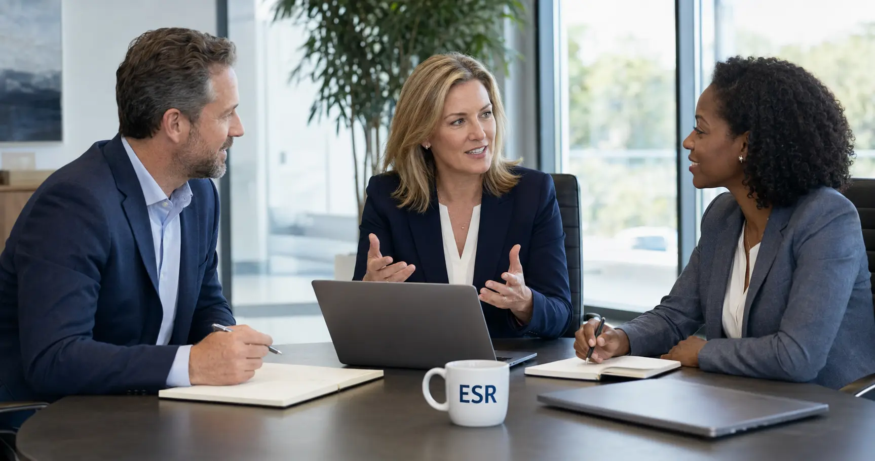 Three business professionals discussing strategy around a conference table with an ESR coffee mug